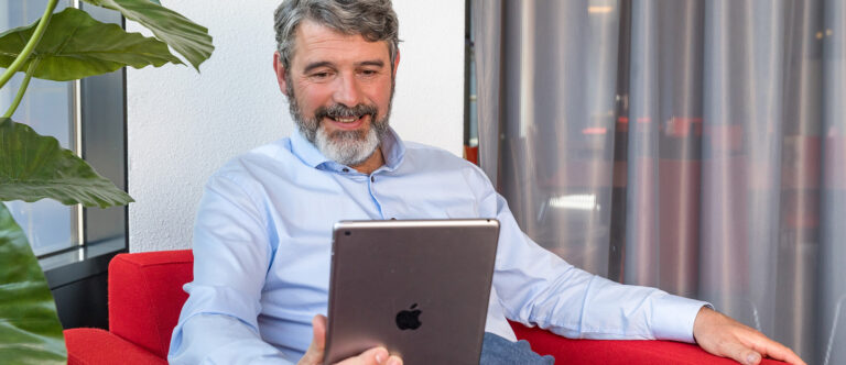 Man kijkt glimlachend naar zijn tablet tijdens een digitaal pre-operatief spreekuur